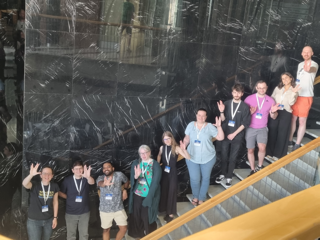 A group of people standing along a staircase holding up the Vulcan salute for SPOC: 'Live long and prosper'. They look relatively happy. Taken at 2024 Galaxy Community Conference.